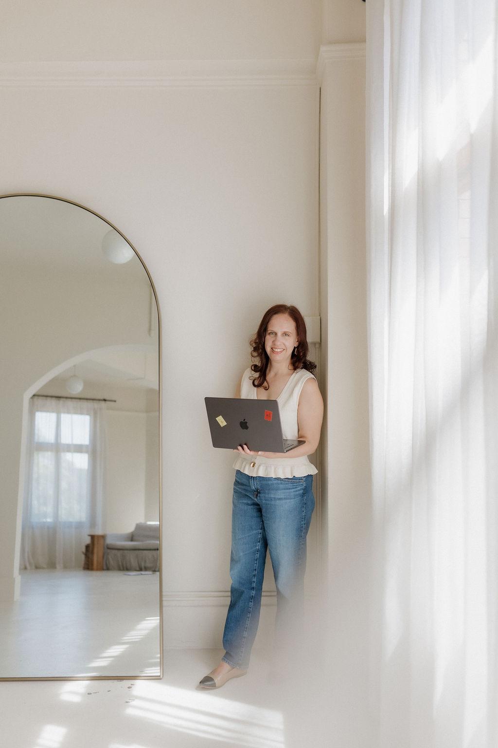 Kathleen standing by a mirror with her laptop