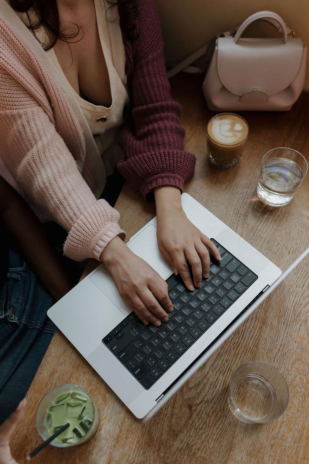 Hands typing on a laptop beside a coffee
